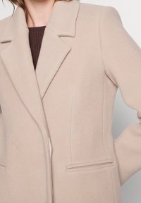 Beige wollen blendjas met een geknipt kraag, zijzakken en een gestructureerde silhoutte, met een zachte, textuurachtige afwerking.