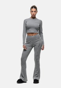 Grijze geribbelde cropped top en uitlopende broek met een aansluitend ontwerp, voorzien van contrasterende naden en een accent ritsdetail, gecombineerd met zwarte schoenen.