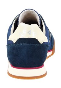 Marineblaue Sneaker mit einem Wildleder-Fersenbereich und cremefarbenen Akzenten, auf denen "1949" in Silber geprägt ist. Flache Gummisohle mit roten Details. Texturiertes Innenfutter.