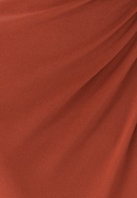Rustfarvet stof med en glat overflade, der har bløde draperinger og en subtil glans. Ingen synlige mønstre eller hardwaredetaljer.