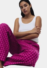 Różowe w kratę spodnie od piżamy z elastycznym pasem i detalem z guzików, w połączeniu z dopasowanym białym topem na ramiączkach. Gładka faktura tkaniny.