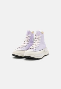 Sneakers alte in tela lavanda con suola in gomma crema, cappuccio bianco e badge rotondo; presentano lacci bianchi e tomaia texturizzata.