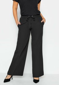 Pantaloni neri a gamba larga realizzati in un tessuto morbido, con vita elasticizzata e cordino, e tasche laterali. Texture liscia, design casual.