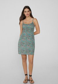 Vestido sin mangas verde con un patrón de paisley en rosa y azul, que presenta un corsé ajustado y una falda acampanada, hecho de tela ligera.