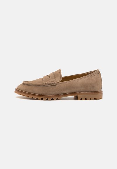 Suede loafers in light brown with a textured finish, featuring a decorative strap across the vamp and a rugged rubber sole for traction.