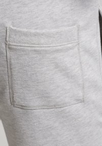 Bolsillo de tela gris claro con borde superior acanalado, cosido a un material de tela texturizada a juego.