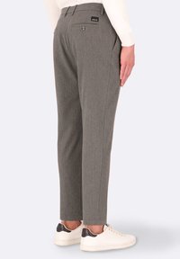 Pantaloni grigi su misura con una texture liscia, dotati di una tasca posteriore e di un'etichetta con il marchio. Abbinati a sneakers bianche.