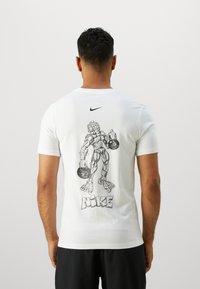 Camiseta de algodón blanca con un gráfico negro de una figura musculosa sosteniendo pesas, con el texto "NIKE" debajo de la imagen y un logo en el pecho.