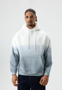 Capuchontrui met een verloopontwerp dat wit mengt naar lichtblauw. Voorzien van een voorzak en trekkoordsluitingen. Zachte stoftextuur.