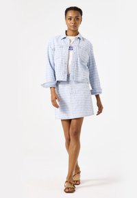Conjunto de chaqueta y falda de mezclilla azul claro con un sutil patrón texturizado. Cuenta con una chaqueta corta con botones y una falda de talle alto.