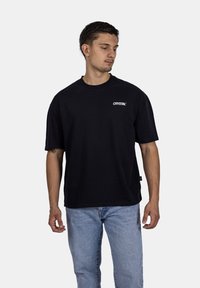 Černé bavlněné tričko s krátkým rukávem, kulatým výstřihem, se malým bílým logem "CRYSTAL" na levé části hrudi a štítkem na boční straně.