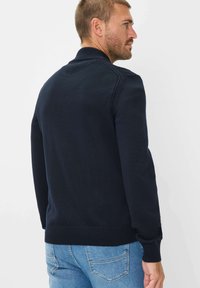 Maglione a collo alto di colore blu navy lavorato a maglia, con polsini e orlo a coste. Presenta dettagli sulle maniche e una texture liscia.