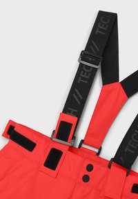 Röda snöbyxor med svarta justerbara hängslen med en logotyp, Velcro-detaljer och två svarta knappar fram. Slät textur.