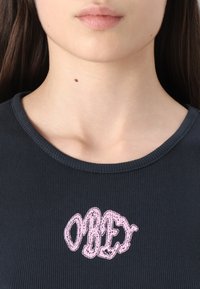 Black ribbed shirt with a round neckline featuring pink embroidered text "OBEY" at the center. Smooth texture with subtle stretch.