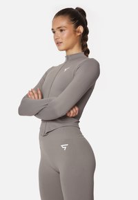 Gray fitted athletic top with a high collar and zip closure, paired with matching leggings featuring a subtle logo on the side.