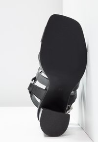 Sandale noire à talon haut avec plusieurs lanières horizontales, texture en cuir lisse et un talon arrondi. Taille 37 indiquée sur la semelle.