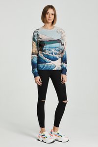 Erinevate värvidega pika varrukaga sweatshirts, millel on mägede ja lainete muster, valmistatud siledast kangast, kombineeritud mustade rebitud kitsaste teksade ja spordijalatsitega.