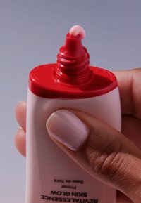 Weiße Tube mit rotem Deckel, ausgestattet mit einer Pipettenspitze, die eine hellrosa Creme abgibt, gehalten in einer Hand mit einem hellen Nagellack-Finish.