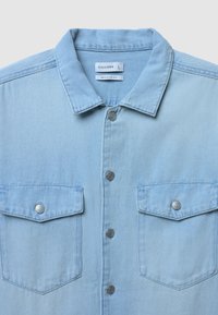 Camicia in denim blu chiaro con colletto a punta, bottoni a pressione argentati, due tasche sul petto e design dalla vestibilità regolare.