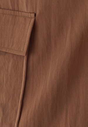 Gros plan sur un tissu marron avec des coutures détaillées et une poche à rabat sur le côté gauche.