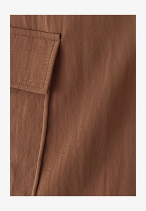 Gros plan sur un tissu marron avec des coutures détaillées et une poche à rabat sur le côté gauche.