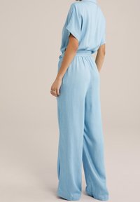 Sininen, löysä haalaripuku, joka on valmistettu pehmeästä kankaasta. Puvussa on kauluspääntie, lyhyet hihat ja joustava vyötärö mukavuutta varten.