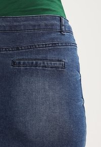 Tummansiniset farkut, joissa on sileä pinta, varustettu takataskulla ja vyölenkillä. Vyötärölinja on hieman lantion yläpuolella.