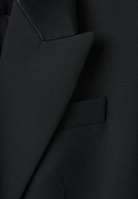 Crni krojeni sako s glatkom, teksturiranom tkaninom, oštrim reverima i jednim džepom na prsima.
