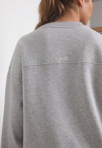 Felpa grigia con vestibilità rilassata, tessuto morbido, collo a coste e sottile ricamo "self." sulla parte superiore della schiena.