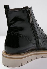 Botín negro de charol con perforaciones decorativas, cremallera lateral, suela texturizada y plataforma de color claro.