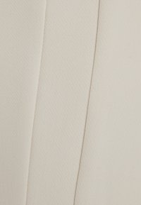 Ljust beige tyg med en texturerad yta, som har en synlig söm och subtila diagonala ribbor, lämpligt för kläder eller stoppning.