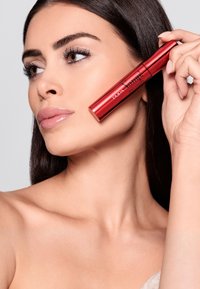 Tubetto di mascara rosso tenuto accanto a un viso con pelle liscia e ciglia lunghe nere, con una finitura lucida e un marchio audace "PUPA VOLUME".