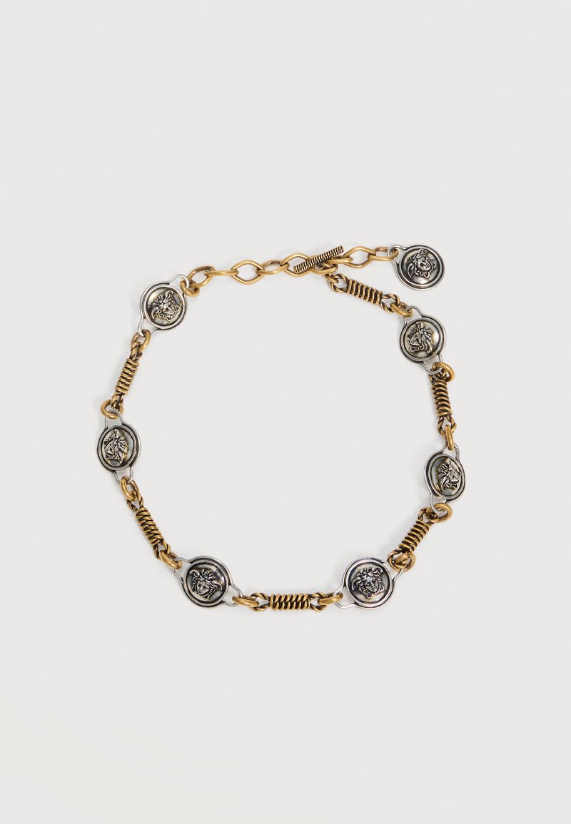 Bracelet chaîne avec des maillons dorés alternant avec des pièces argentées ornées d'une tête de lion en relief, fermé par un fermoir bascule.
