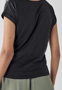 Sort bomulds T-shirt med korte ærmer og oprullede ærmekanter, der har en afslappet pasform og en enkel, glat tekstur. Ingen synlige mønstre eller accenter.