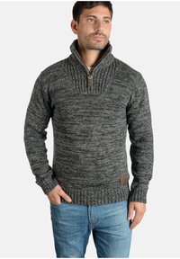 Suéter de punto gris y negro con cremallera de cuarto, con un patrón texturizado, puños y dobladillo acanalados, que presenta un parche de logo de cuero marrón.