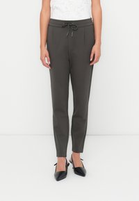 Dunkelgraue maßgeschneiderte Hose mit einer Kordelzugbund, gefältetem Design und glatter Stofftextur, kombiniert mit schwarzen spitzen Schuhen.