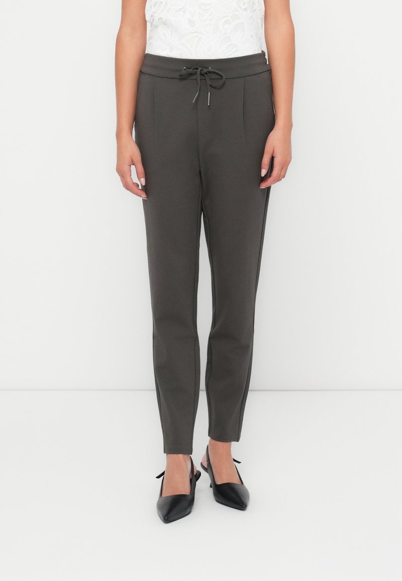 Dunkelgraue maßgeschneiderte Hose mit einer Kordelzugbund, gefältetem Design und glatter Stofftextur, kombiniert mit schwarzen spitzen Schuhen.