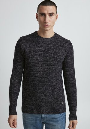 Dark knitted sweater with a textured pattern, crew neck, and ribbed cuffs and hem. Paired with light blue denim jeans.