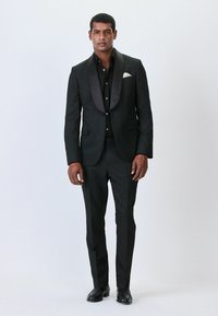 Abito nero con motivo, completo di rever in raso, camicia nera e scarpe lucide. Il completo presenta un design attillato con un tessuto strutturato.