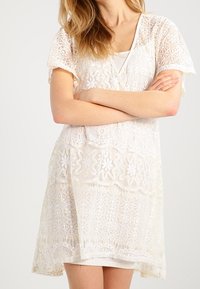 Spetsemorgonrock i vitt, med blommönster och korta ärmar. Lätt och luftig passform. Layered över en linne. Transparent struktur.