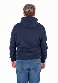 Felpa in cotone blu navy con tasca a canguro e cappuccio con coulisse, abbinata a jeans in denim blu chiaro, vista da dietro.