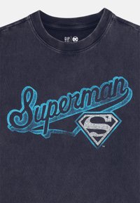 Marineblå bomullströja med en stor turkos "Superman"-skrift och en grå superhjälte-emblem grafik nedanför. Rundhalsad design.