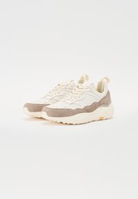 Beige ja taupe värvi sneakersid, millel on erinevad võrkkanga ja seemisnahk tekstuurid, paks valge tald ja tugevdatud kannaosa toe jaoks.