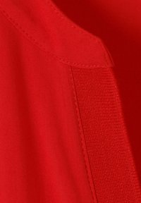 Nahaufnahme von rotem Stoff mit sichtbarem Nähen und einem strukturierten vertikalen Streifen, der entlang einer diagonalen Naht genäht ist.