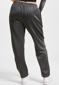 Grå sweatpants med elastisk talje, sidelommer og en tapered fit, parret med hvide sneakers med pink og guld detaljer.