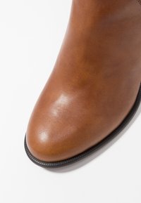 Bruine leren enkelboot met een gladde textuur, ronde teen en zwarte rubberen zool. Heeft een strakke silhouette en minimale accenten.