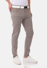 Graue gestreifte Hose im Slim-Fit-Stil, aus strukturierter Stoff gefertigt, mit Fronttaschen und einem weißen Gürtel. Getragen mit weißen Turnschuhen.