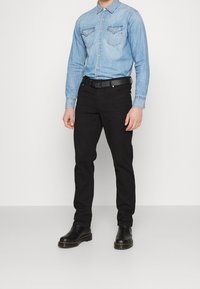 Ljusblå denimskjorta med knapp-down krage och bröstfickor, i kombination med svarta slim-fit byxor och svarta stövlar. Slät textur, avslappnad design.