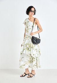 Vestido floral blanco con diseño de un solo hombro, volantes en capas y acentos verdes. Combinado con un bolso cruzado negro y sandalias.