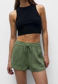 Top corto a coste nero abbinato a pantaloni corti verde testurizzati con vita regolabile e tasche frontali. Design semplice e casual.